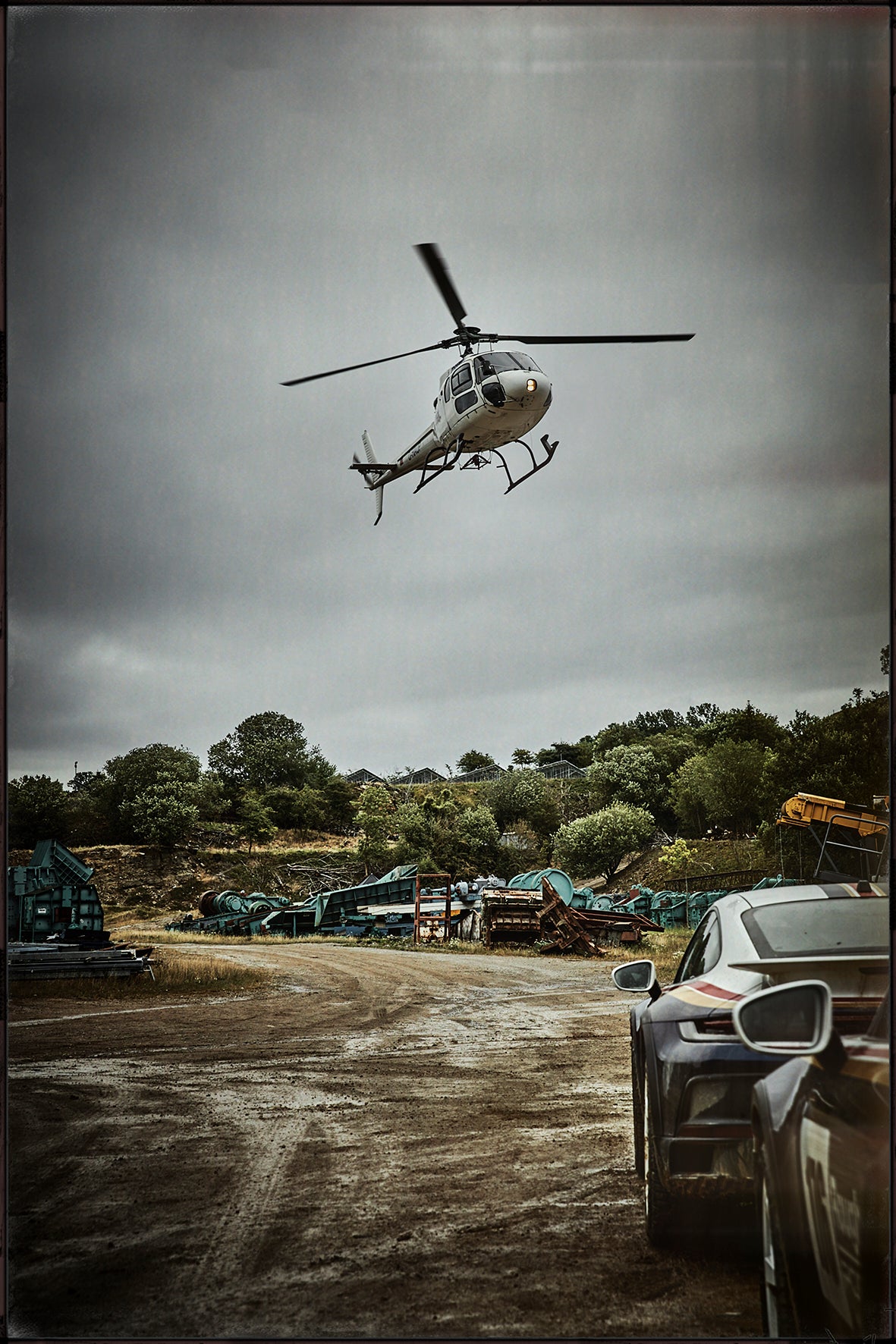 Fine art photo by Frank Kayser – helicopter flying low above rugged terrain with a Porsche in the frame, cinematic atmosphere.