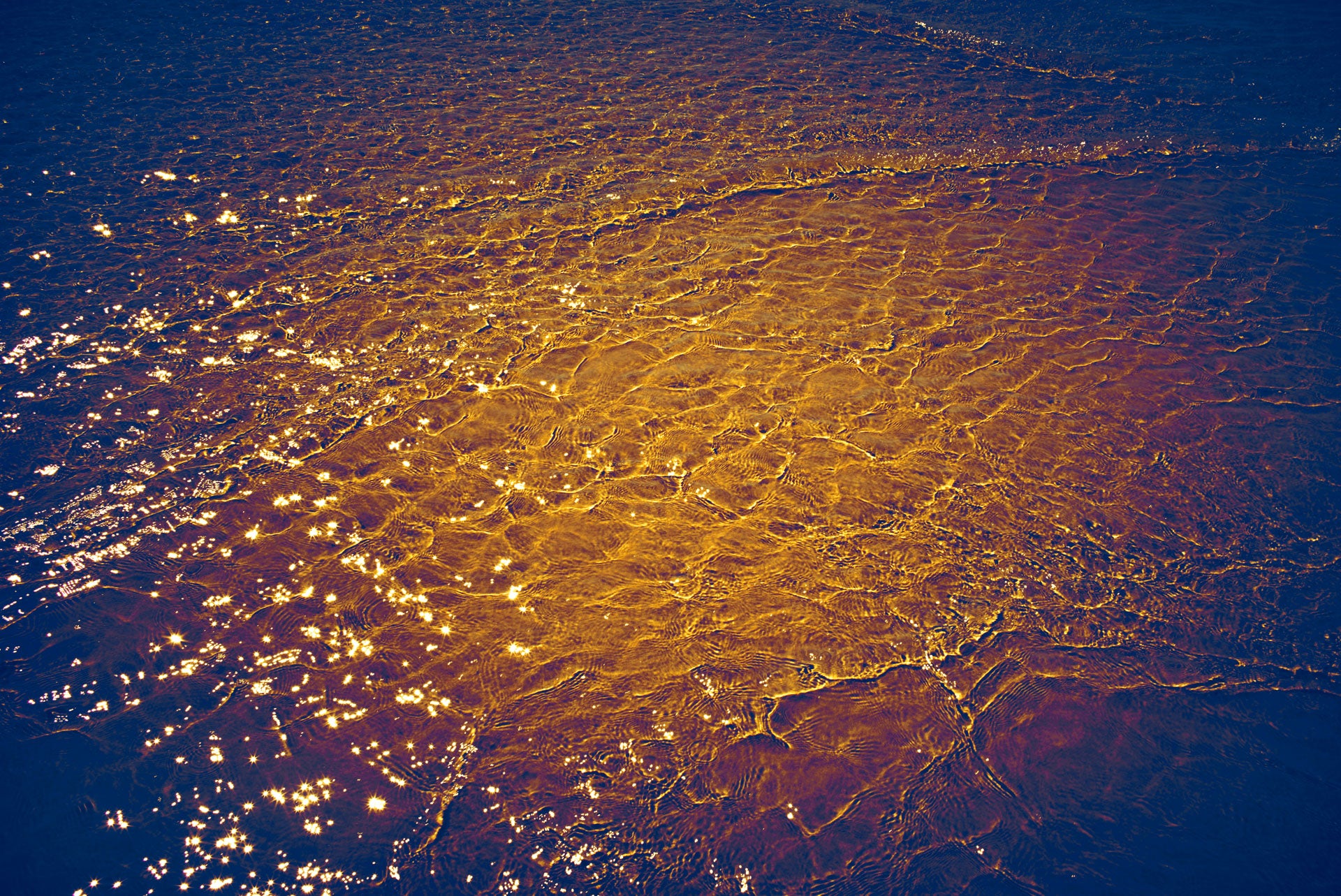 Abstract photograph of golden sunlight reflecting on water waves.