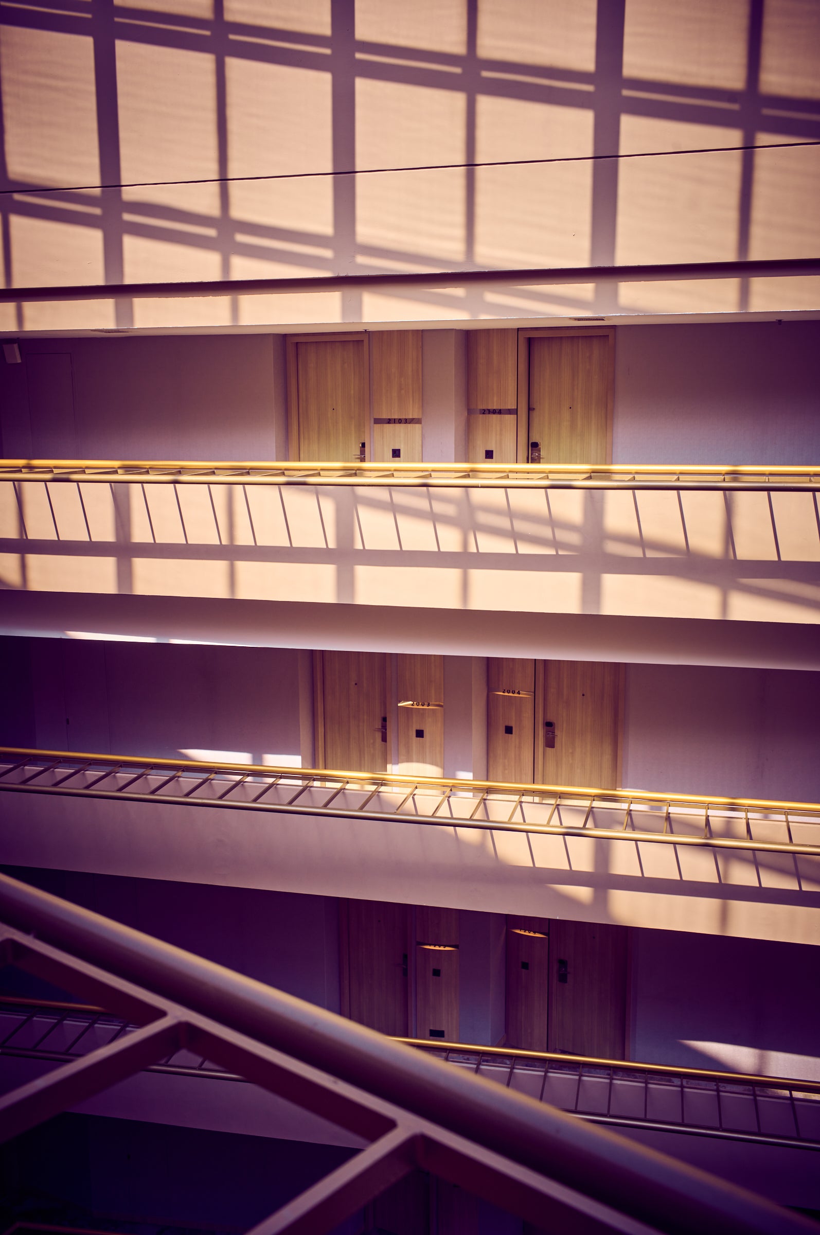 Sunlit atrium with grid shadows, stacked corridors and wooden doors, Singapore — fine art photograph by Frank Kayser.