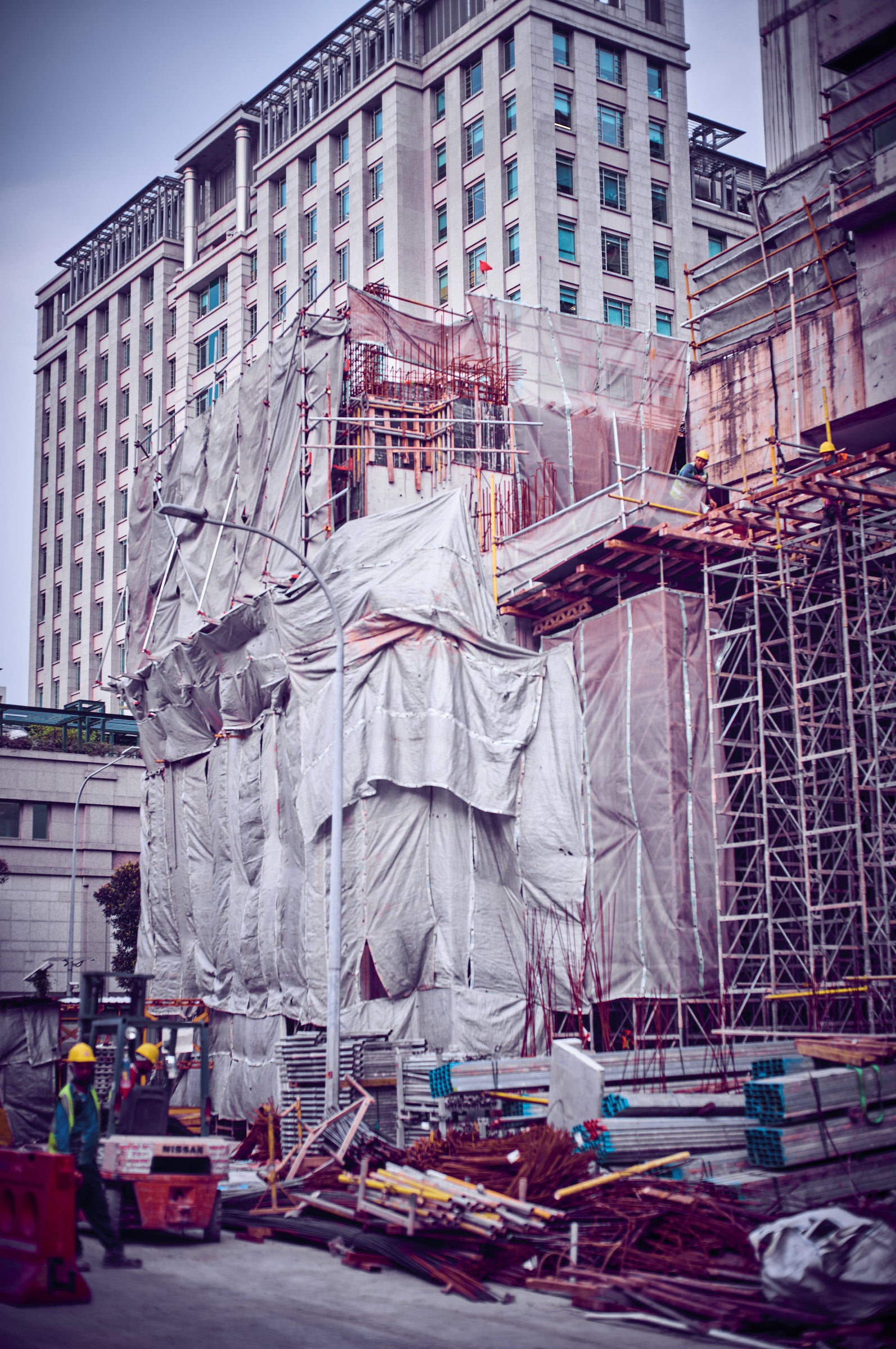 Singapore construction site with tarped scaffolding and rebar before a neoclassical high-rise — photograph by Frank Kayser.