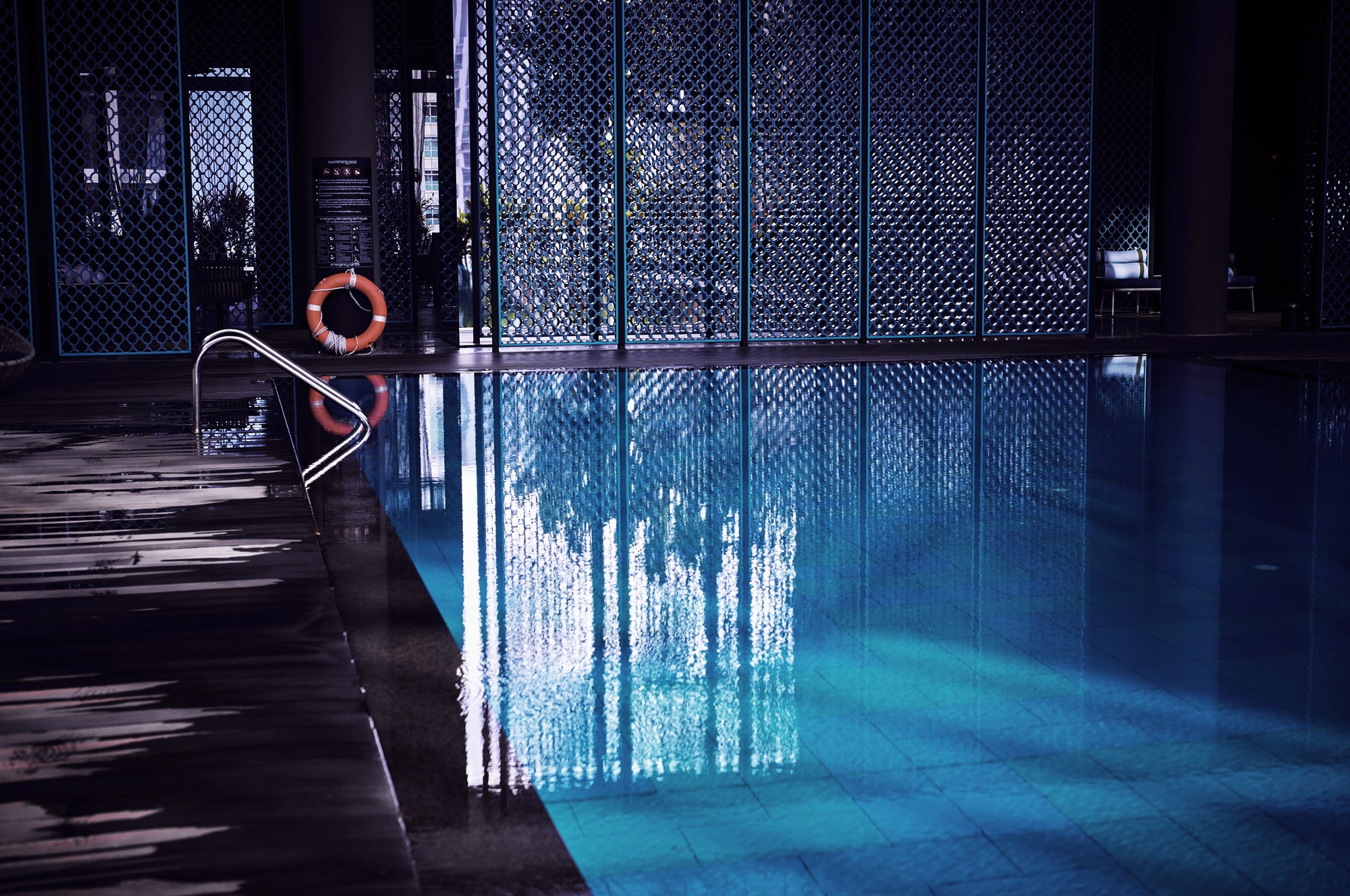 Serene indoor pool in Singapore with geometric lattice screens and blue reflections, fine art photograph by Frank Kayser.