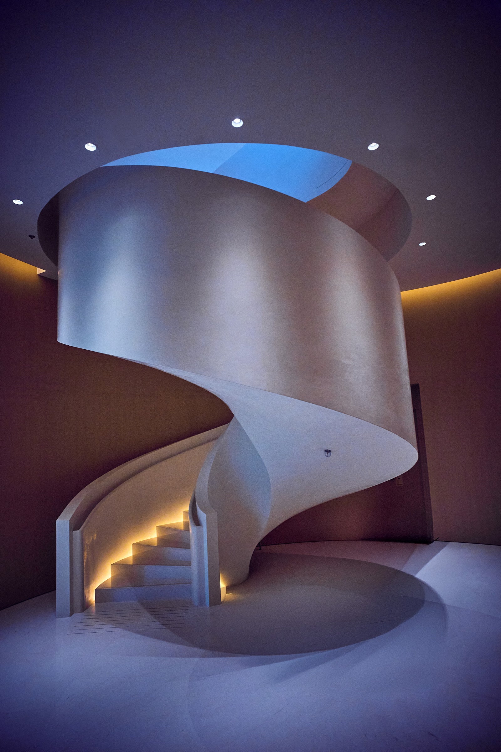 Fine art architectural photography by Frank Kayser – futuristic spiral staircase with soft lighting and blue ceiling opening, minimalistic design, limited edition wall art.