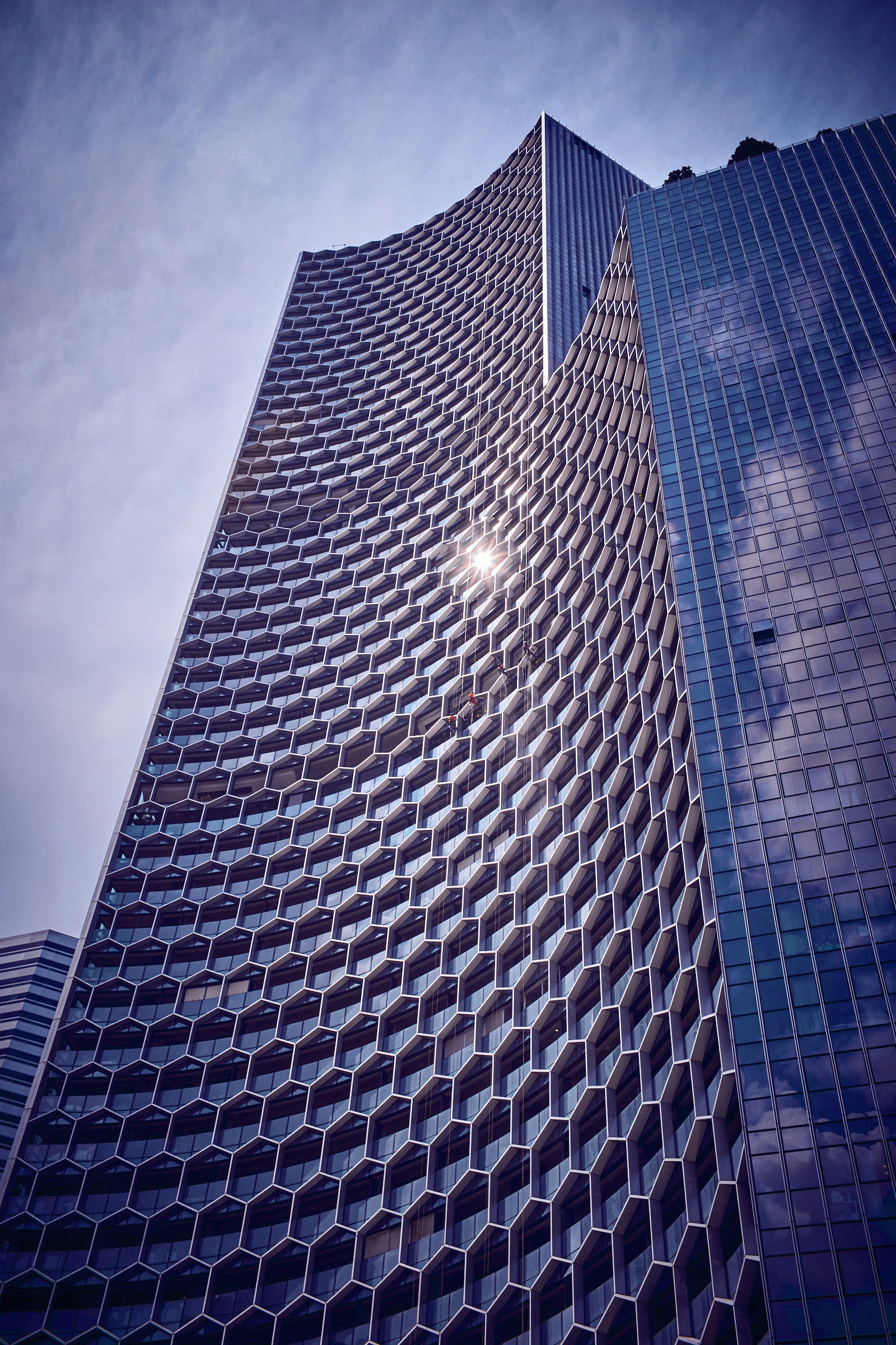 Honeycomb façade high-rise in Singapore with sun flare and suspended window cleaners, fine art photo by Frank Kayser.