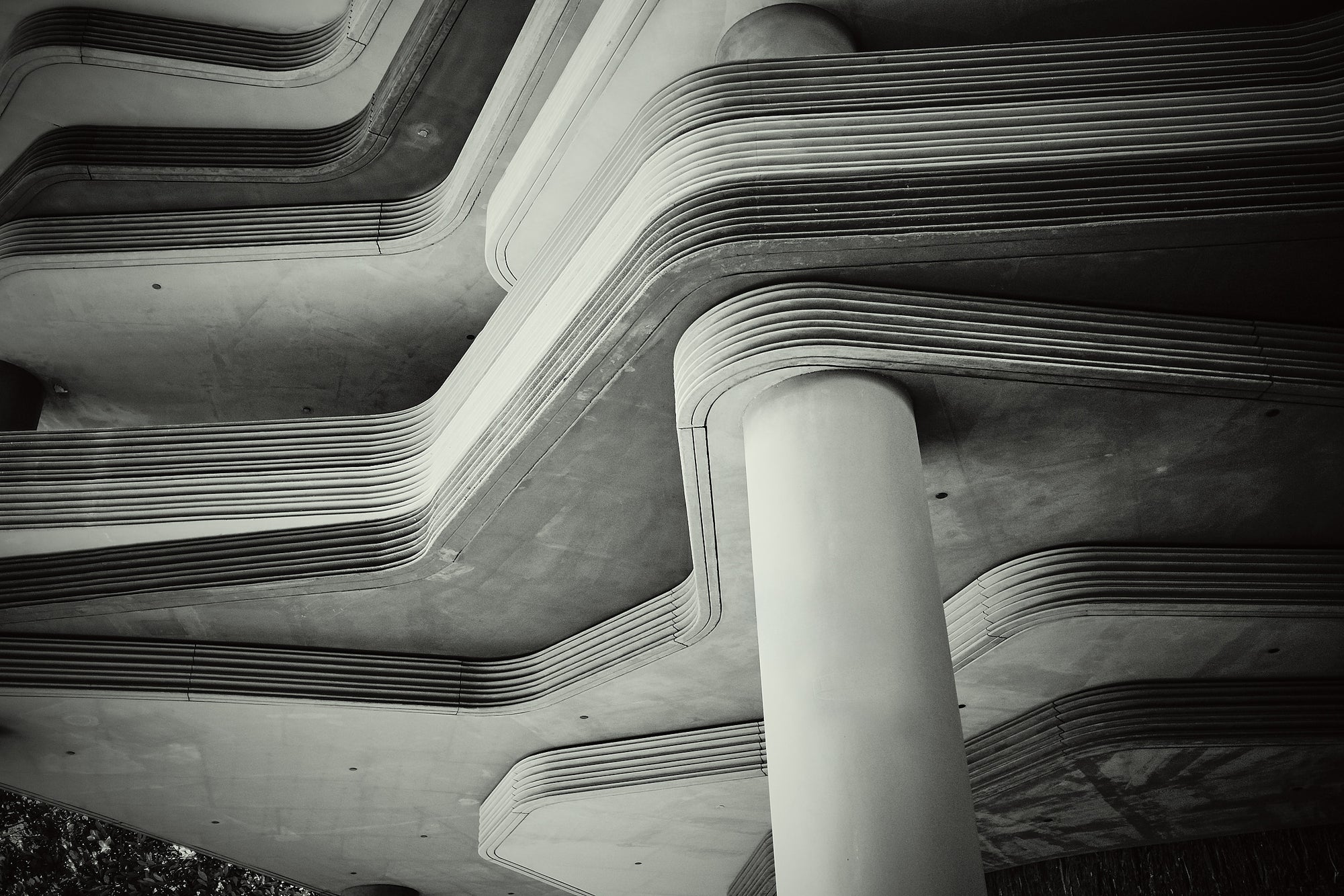 Monochrome layered concrete decks with rounded edges and a cylindrical column, architectural detail, Singapore.