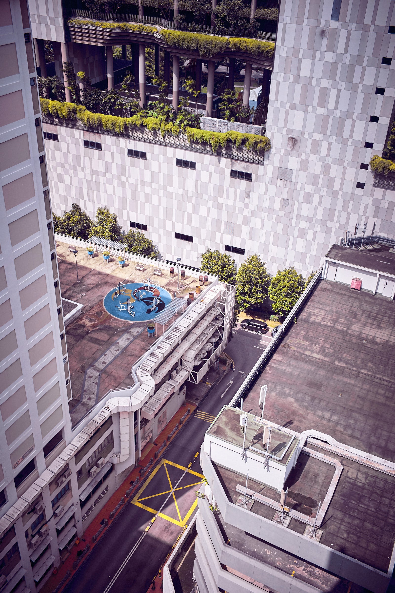 Rooftop playground and service ducts between high-rises, aerial view with yellow road grid, Singapore.