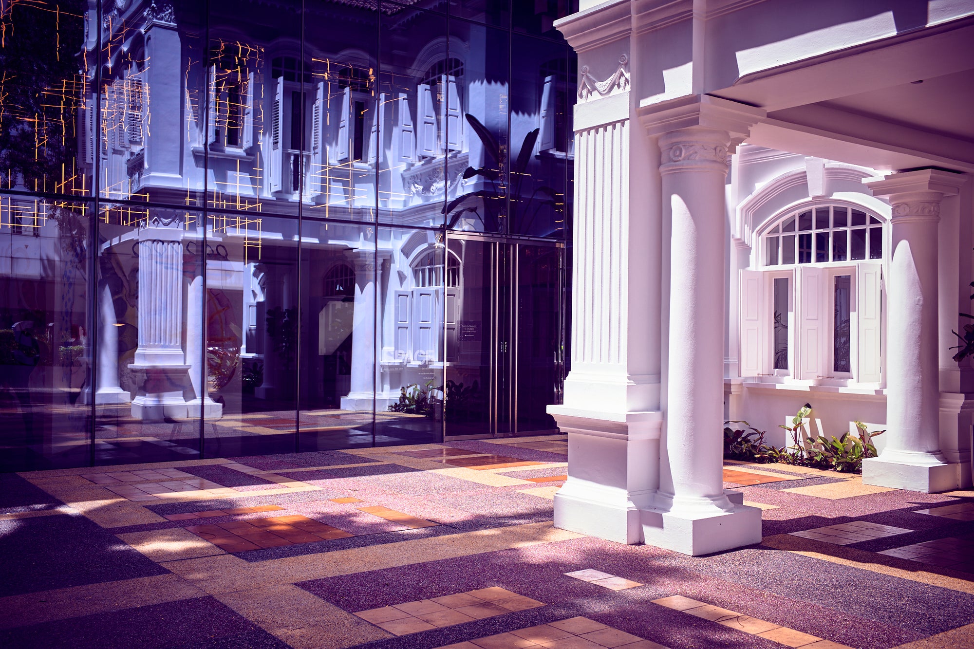 Colonial white colonnade and glass façade reflection with patterned courtyard, Singapore.
