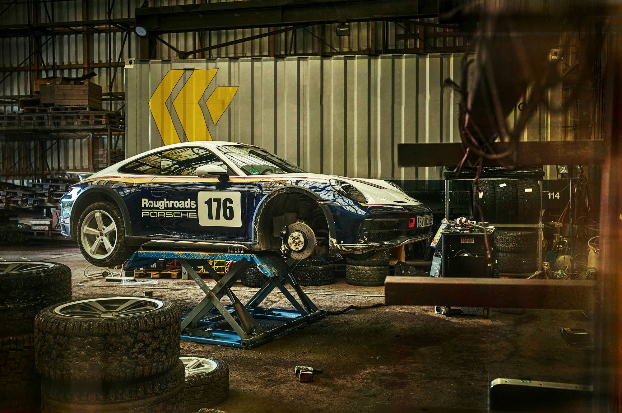 Fine art photography by Frank Kayser – Porsche 911 Dakar undergoing service, mechanics and dust in the background.