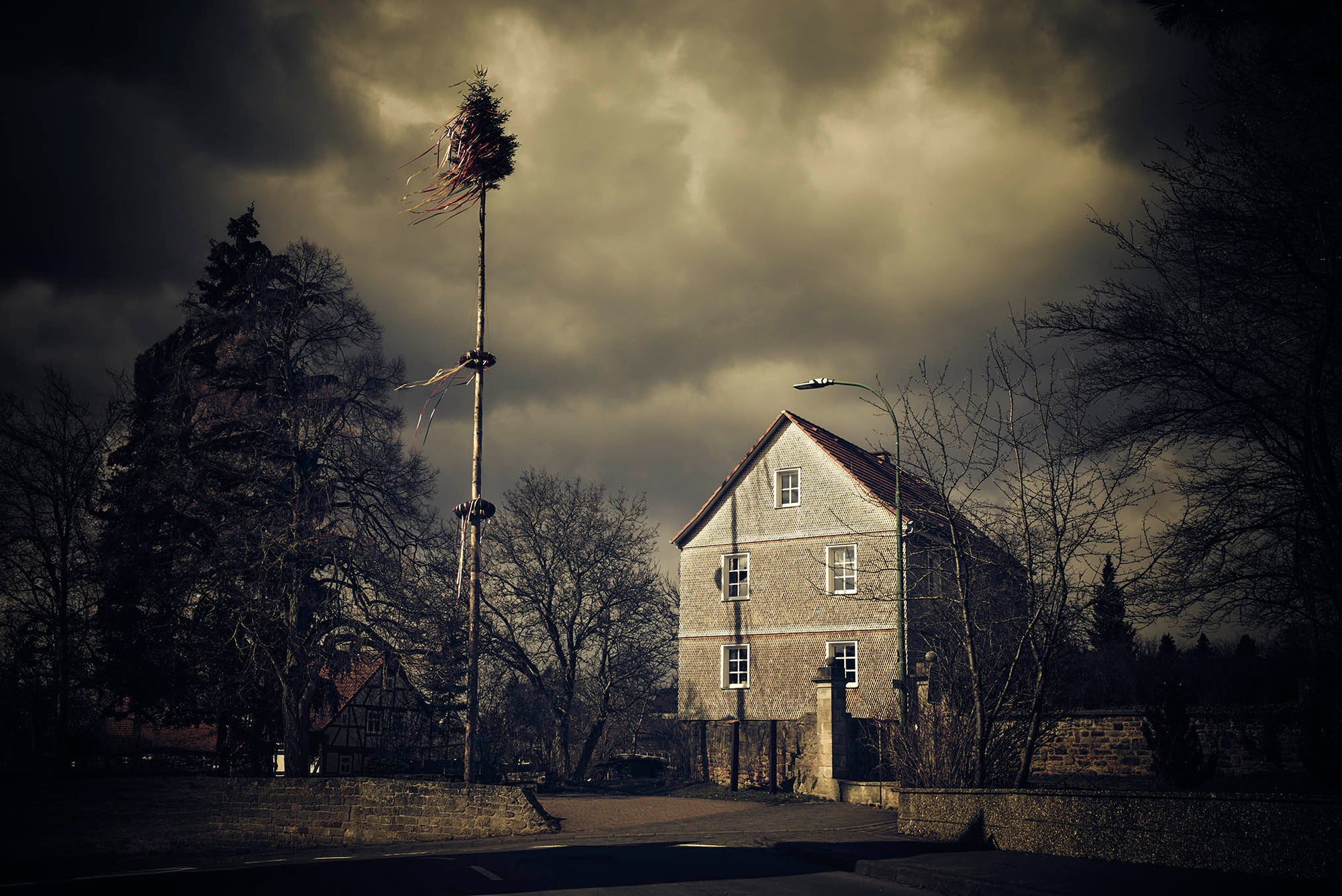 Fine art photography by Frank Kayser – a Kirmesbaum (maypole) swaying in the wind against dramatic skies in a Rhön village, symbol of local festivities.