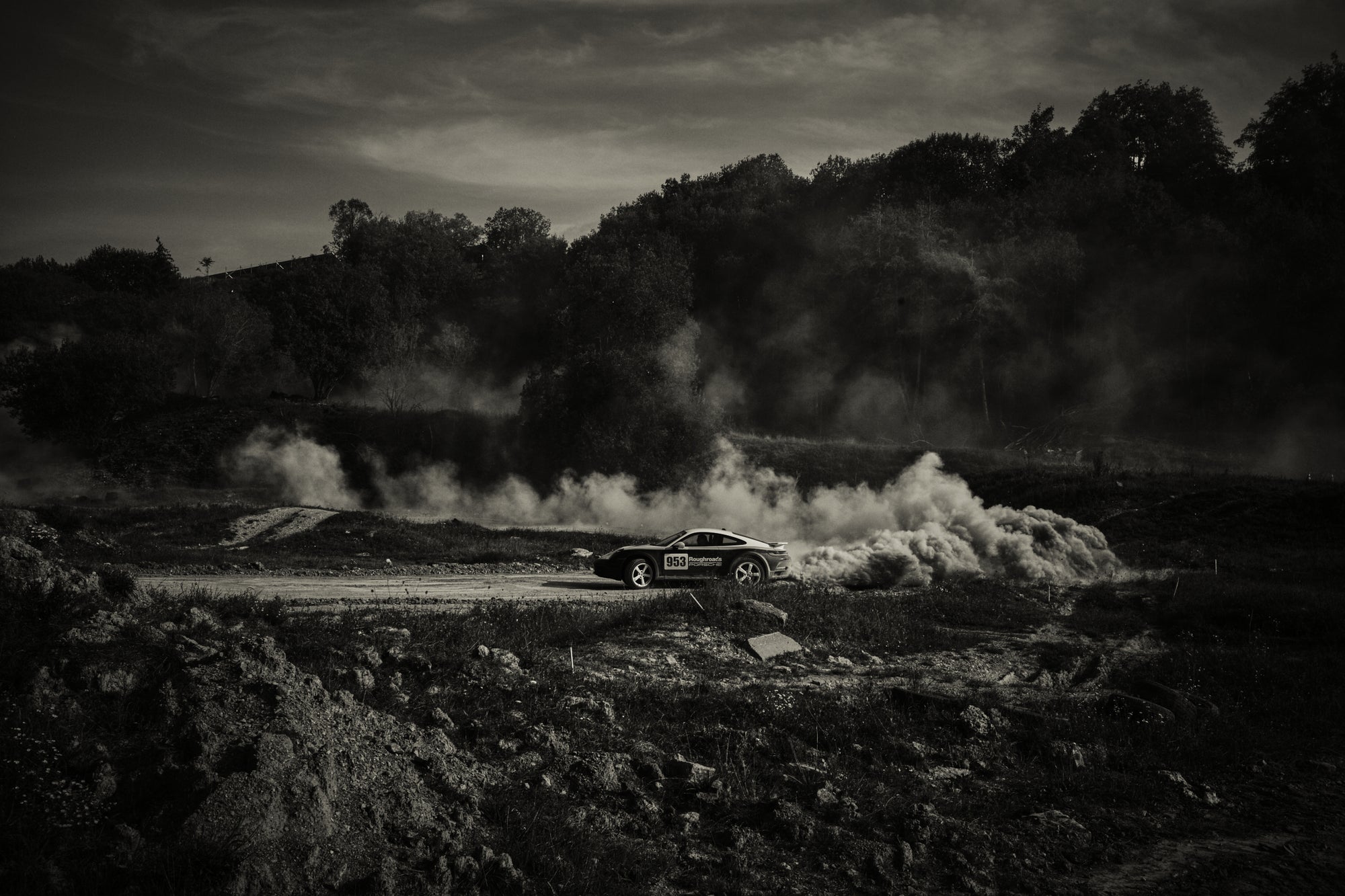 Fine art photography by Frank Kayser – Porsche 911 Dakar speeding through a gravel road, leaving behind a massive trail of dust clouds in a dark landscape.