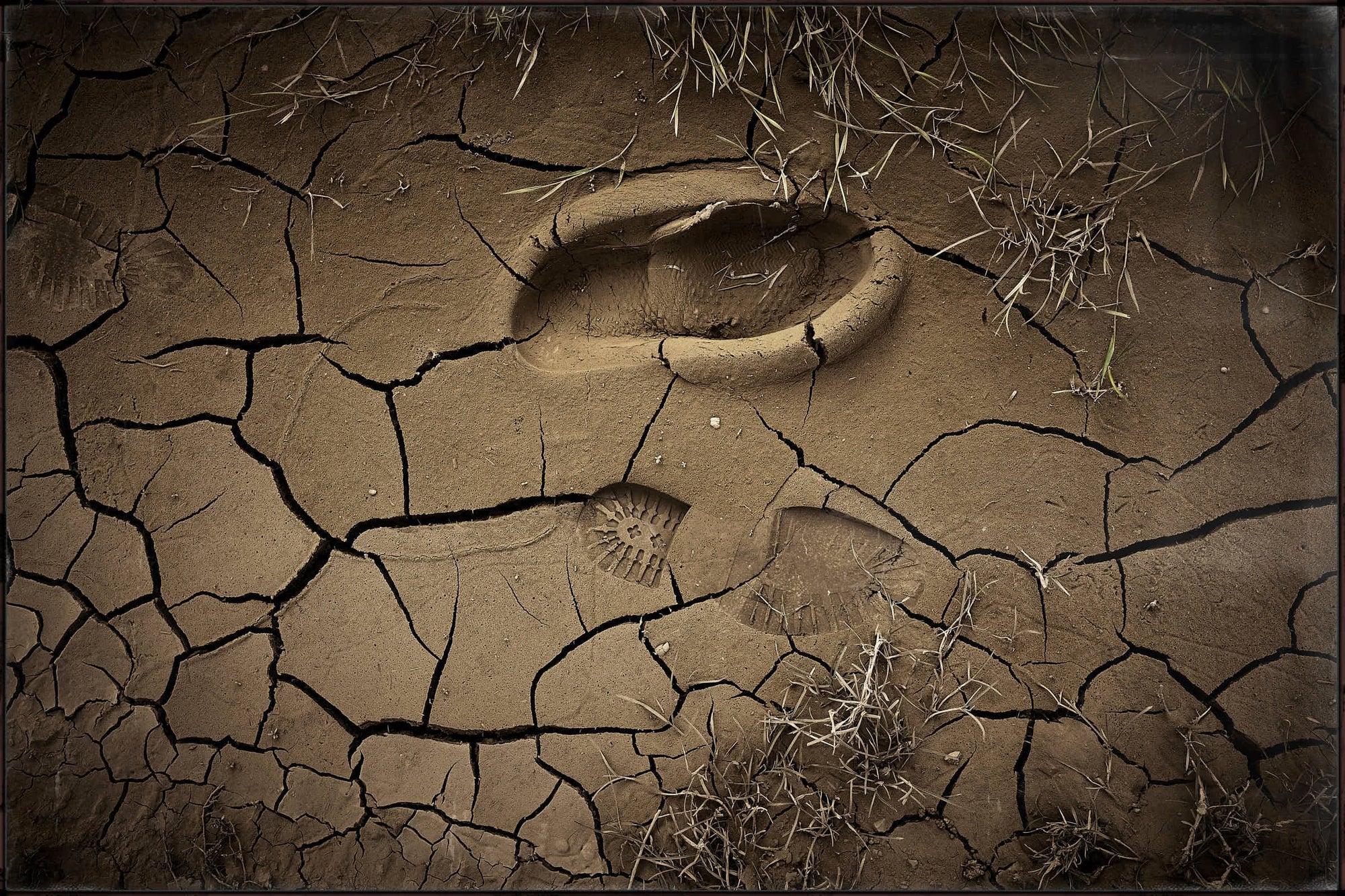 Fine art photo by Frank Kayser – footprints embedded in cracked dry mud, traces of Dakar adventure.