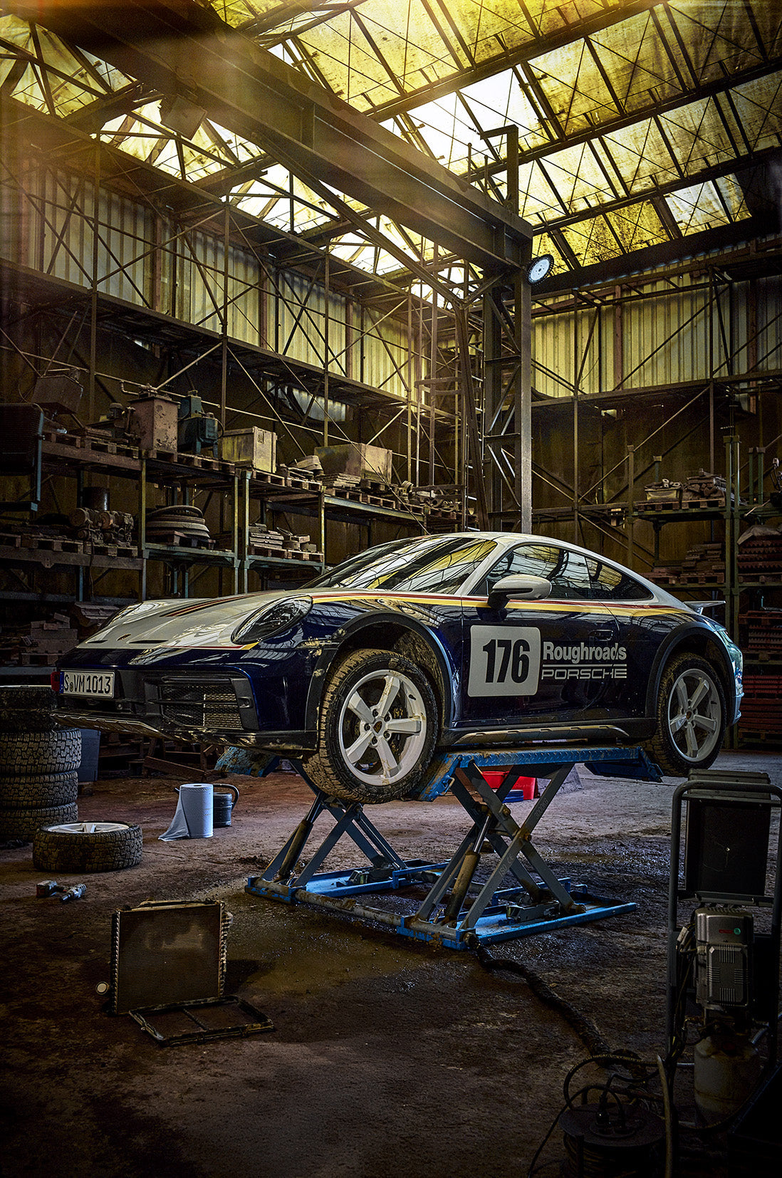 Fine art photography by Frank Kayser – Porsche 911 Dakar on a lift inside an industrial workshop, dramatic light and raw setting.