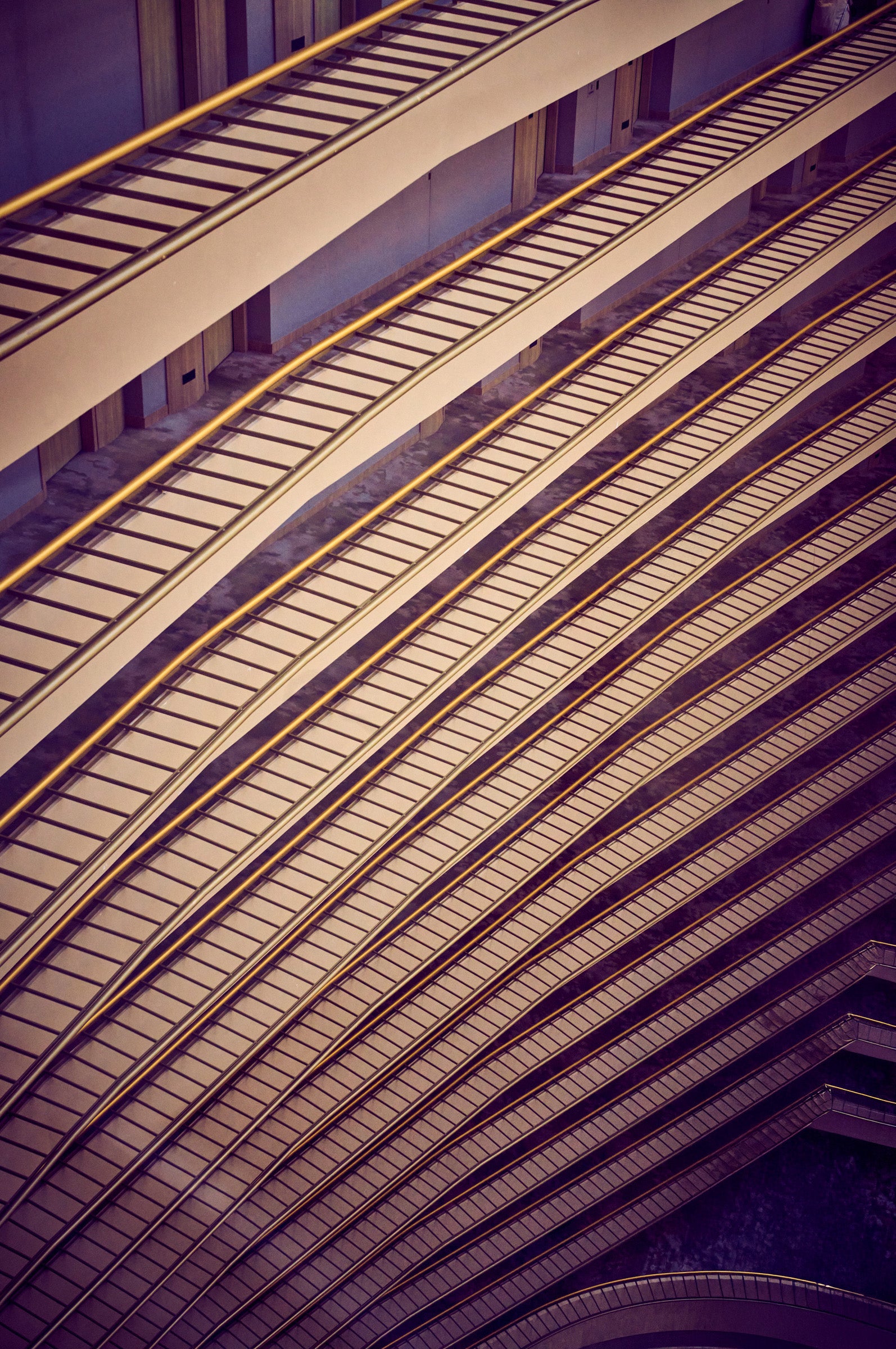 Diagonal pattern of stacked atrium balconies with golden rails and ladder-like shadows, Singapore.
