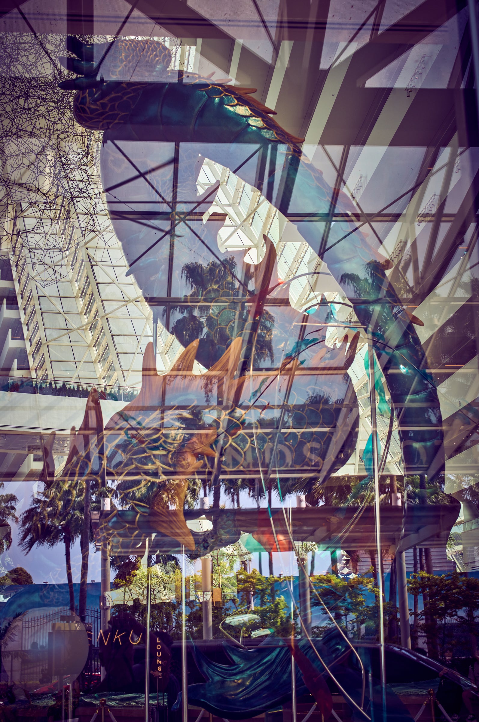 Layered glass reflections with mythical dragon motif, palms and atrium geometry, Singapore.
