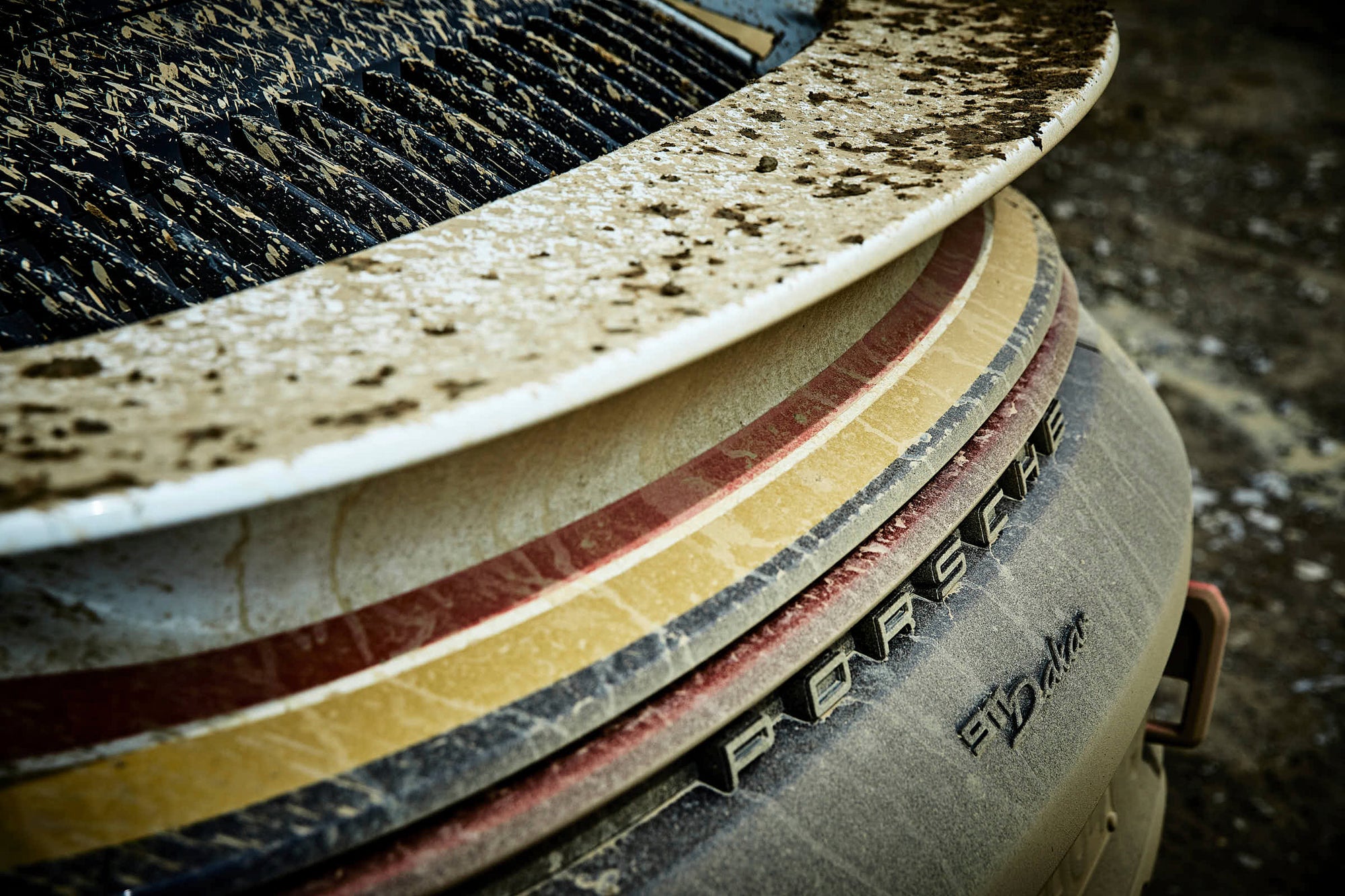 Verschmutzter Heckspoiler mit Farbstreifen und Porsche-Schriftzug, Close-up in der Kiesgrube.