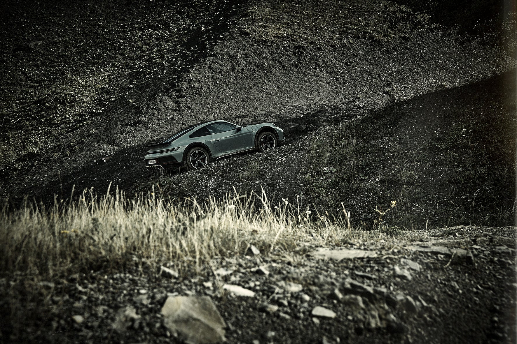 Offroad-Aufstieg eines 911, trockene Gräser im Vordergrund, Geröllhänge im Hintergrund.